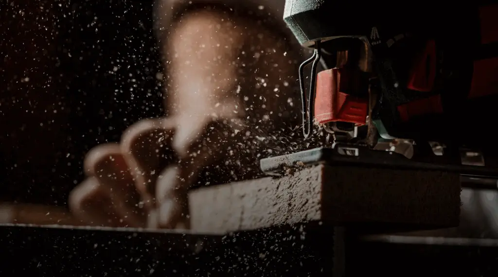 Close-up of a jigsaw cutting through wood with sawdust flying in the air.