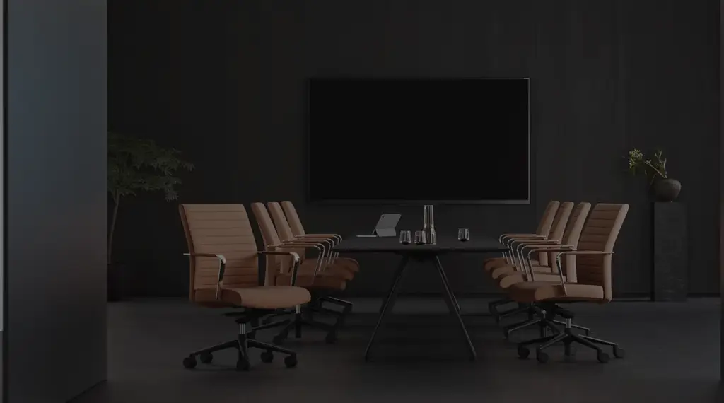 A modern, minimalist conference room with brown leather chairs surrounding a dark table, featuring a large blank screen on a black wall in the background.
