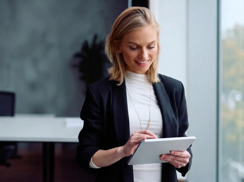 A professional woman smiling while working on a tablet in a modern office.