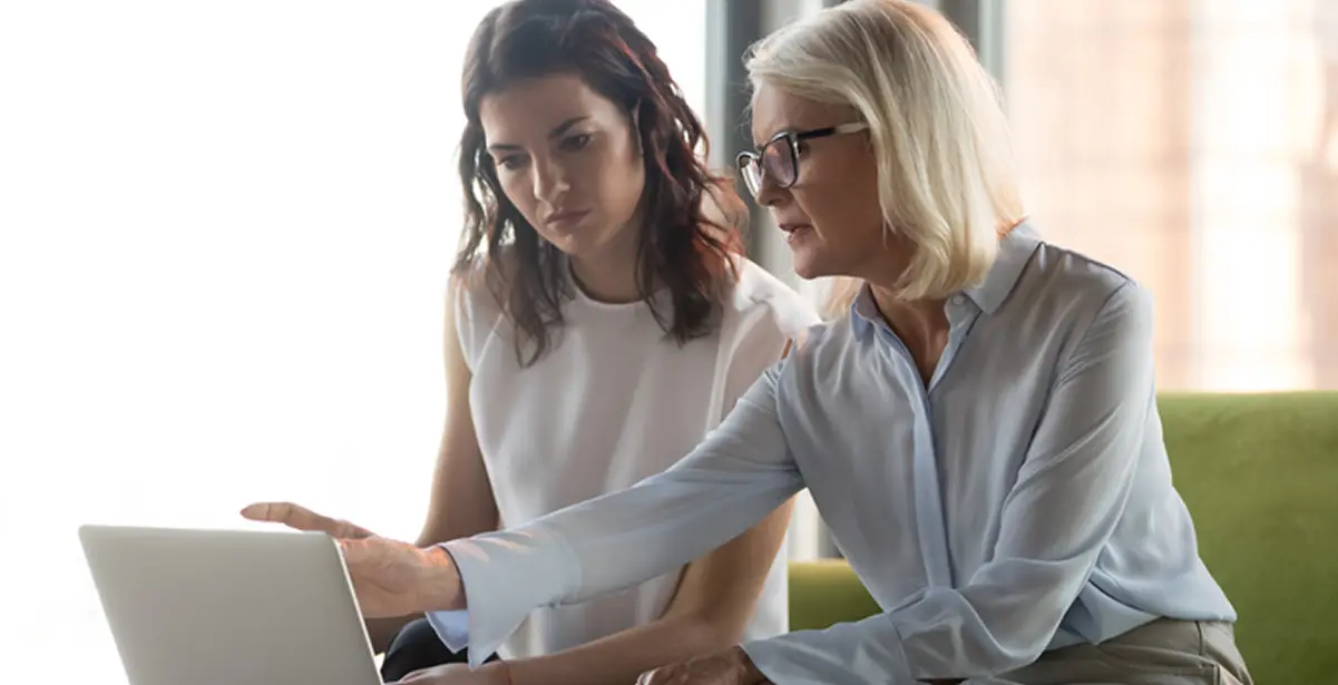 Two female professionals collaborating and reviewing data on a laptop.